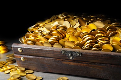 Image of Open treasure chest with gold coins on grey wooden table, closeup 