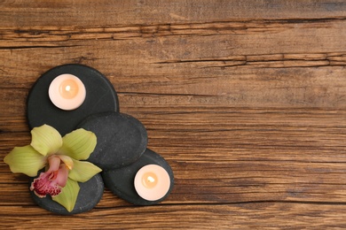 Photo of Pile of spa stones with lit candles and flower on wooden background, flat lay. Space for text