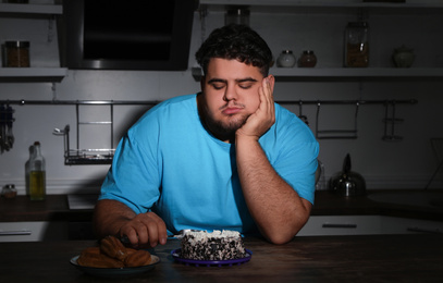 Depressed overweight man eating cake in kitchen at night