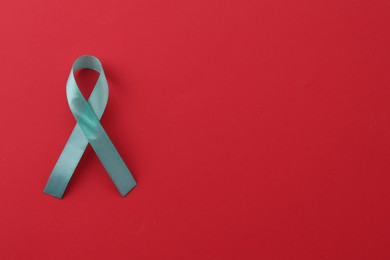 Photo of Turquoise awareness ribbon on red background, top view. Space for text