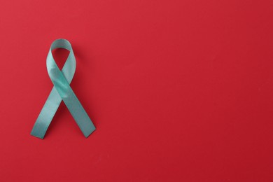 Turquoise awareness ribbon on red background, top view. Space for text