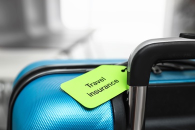 Blue suitcase with TRAVEL INSURANCE label indoors, closeup