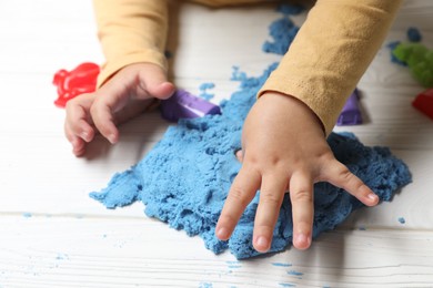 Little child playing with light blue kinetic sand at white wooden table, closeup