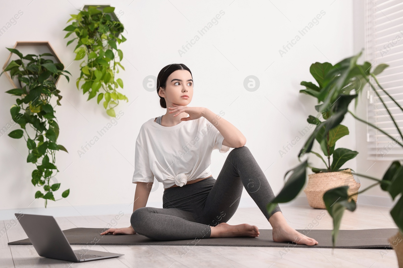 Photo of Beautiful girl sitting on yoga mat near laptop in studio