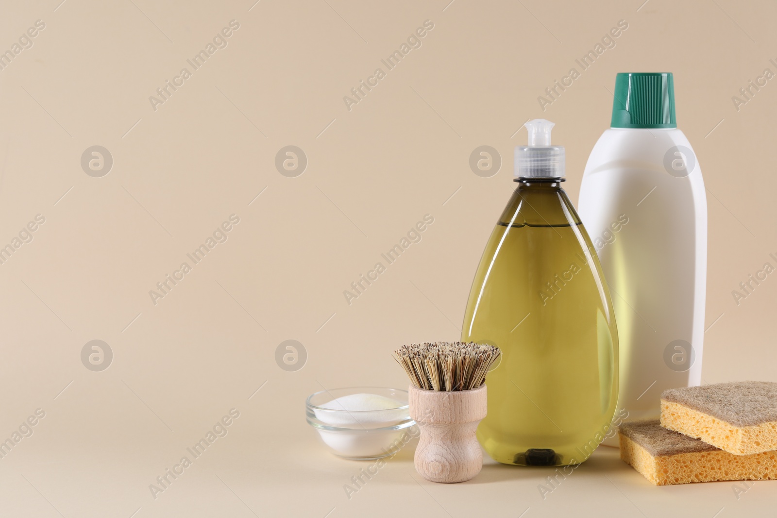 Photo of Bottles of cleaning product, brush, sponges and baking soda on beige background. Space for text