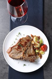 Delicious fried beef meat, vegetables and wine on grey table, top view