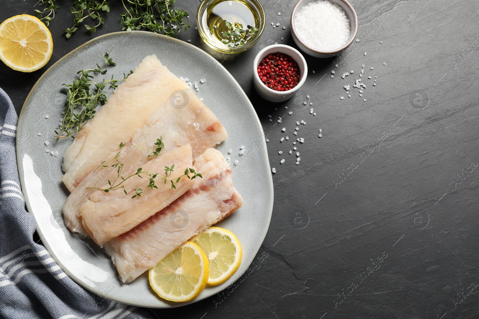 Photo of Plate with raw cod fish, microgreens, spices and lemon on dark textured table, flat lay. Space for text