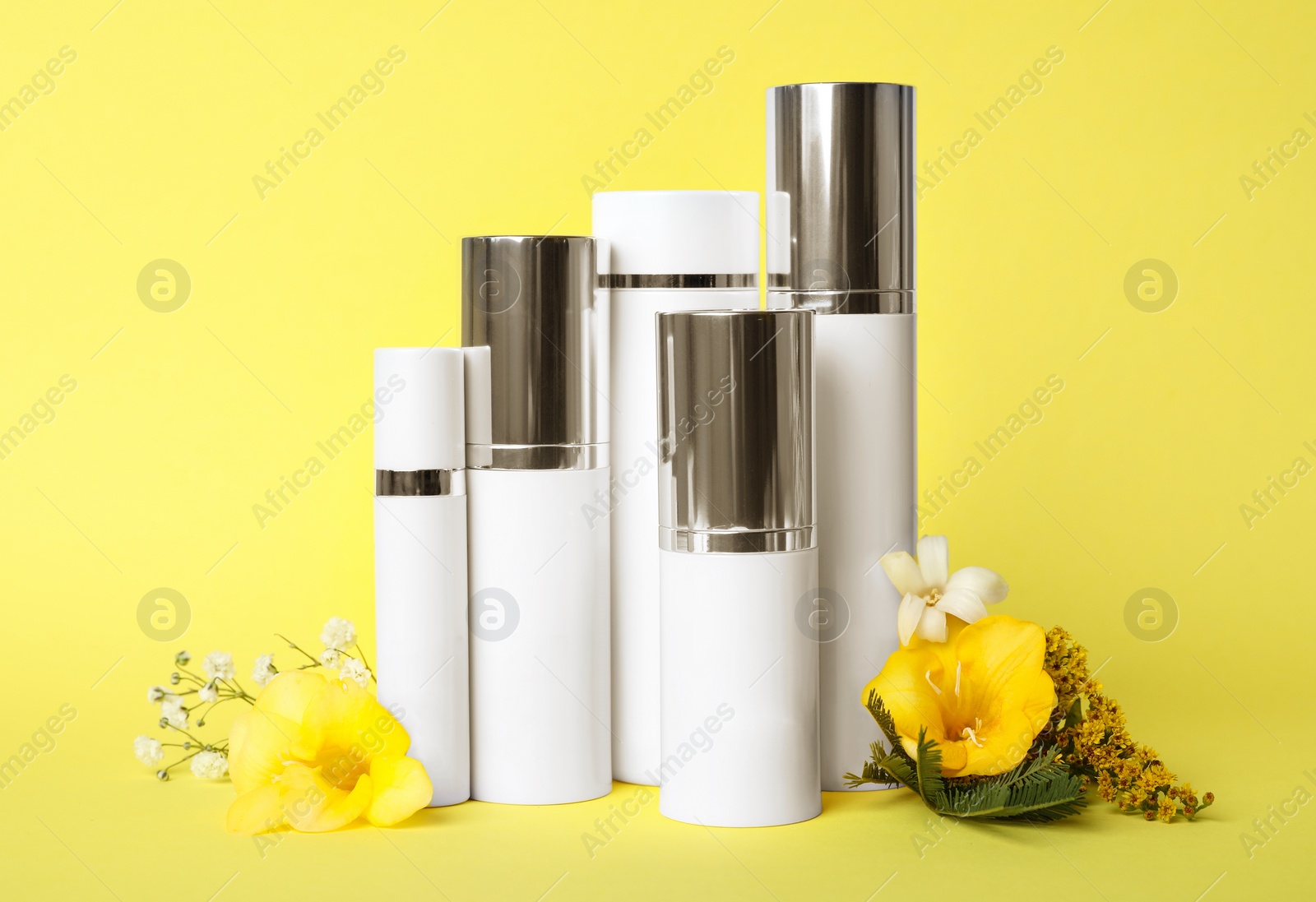 Photo of Set of luxury cosmetic products and flowers on yellow background