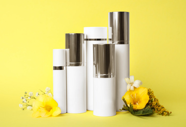 Photo of Set of luxury cosmetic products and flowers on yellow background
