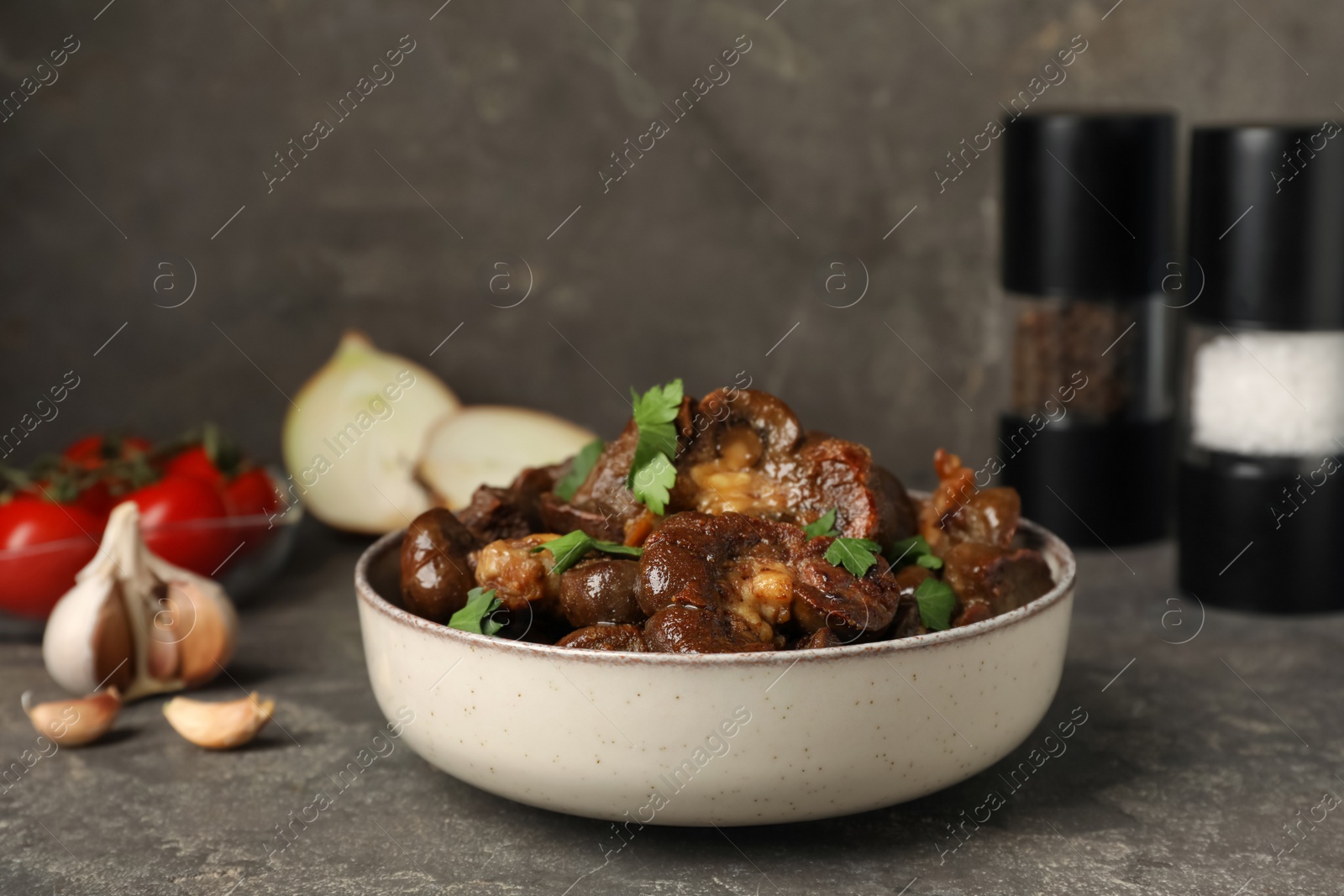 Photo of Bowl with delicious kidneys and parsley on grey table