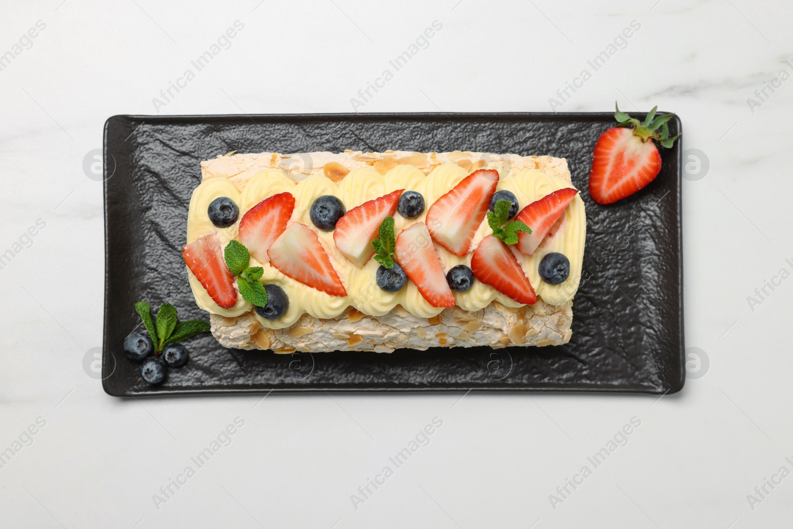 Photo of Tasty meringue roll with cream, strawberry, blueberry and mint on white marble table, top view