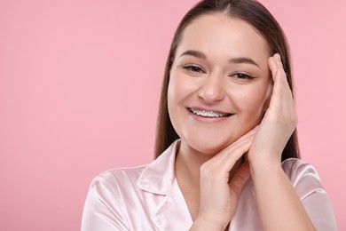 Smiling woman with dental braces on pink background. Space for text