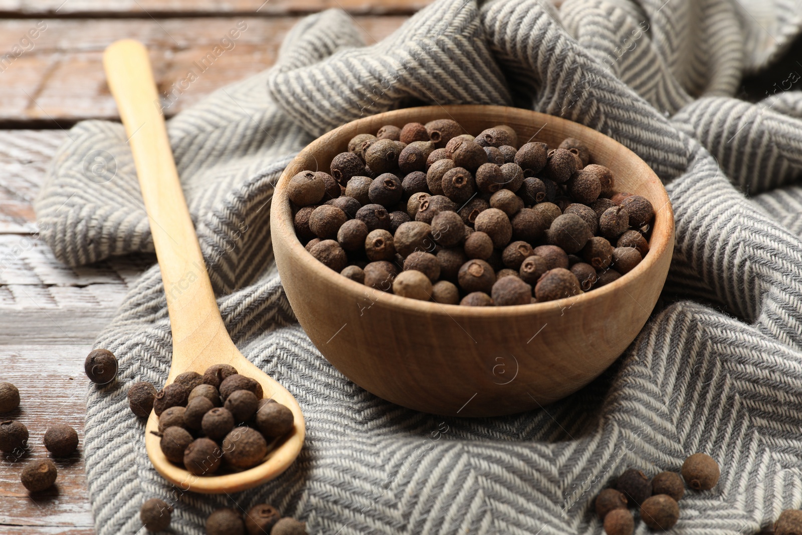 Photo of Aromatic allspice pepper grains in bowl and spoon on wooden table