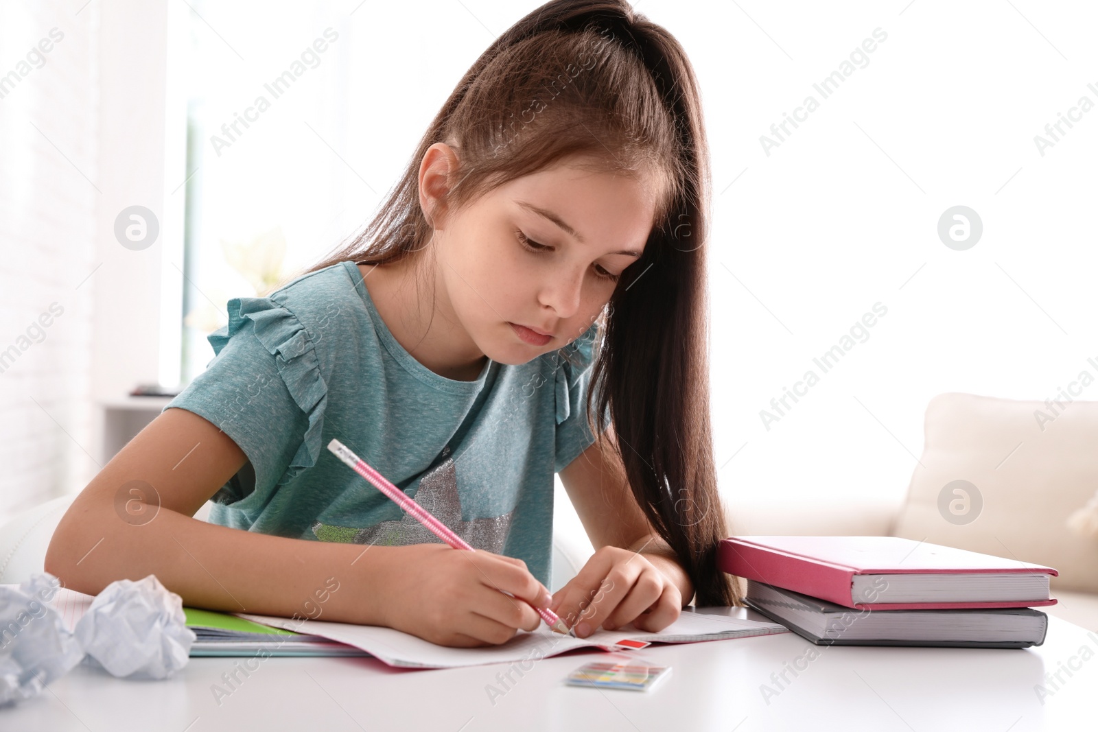 Photo of Pretty preteen girl doing homework at table