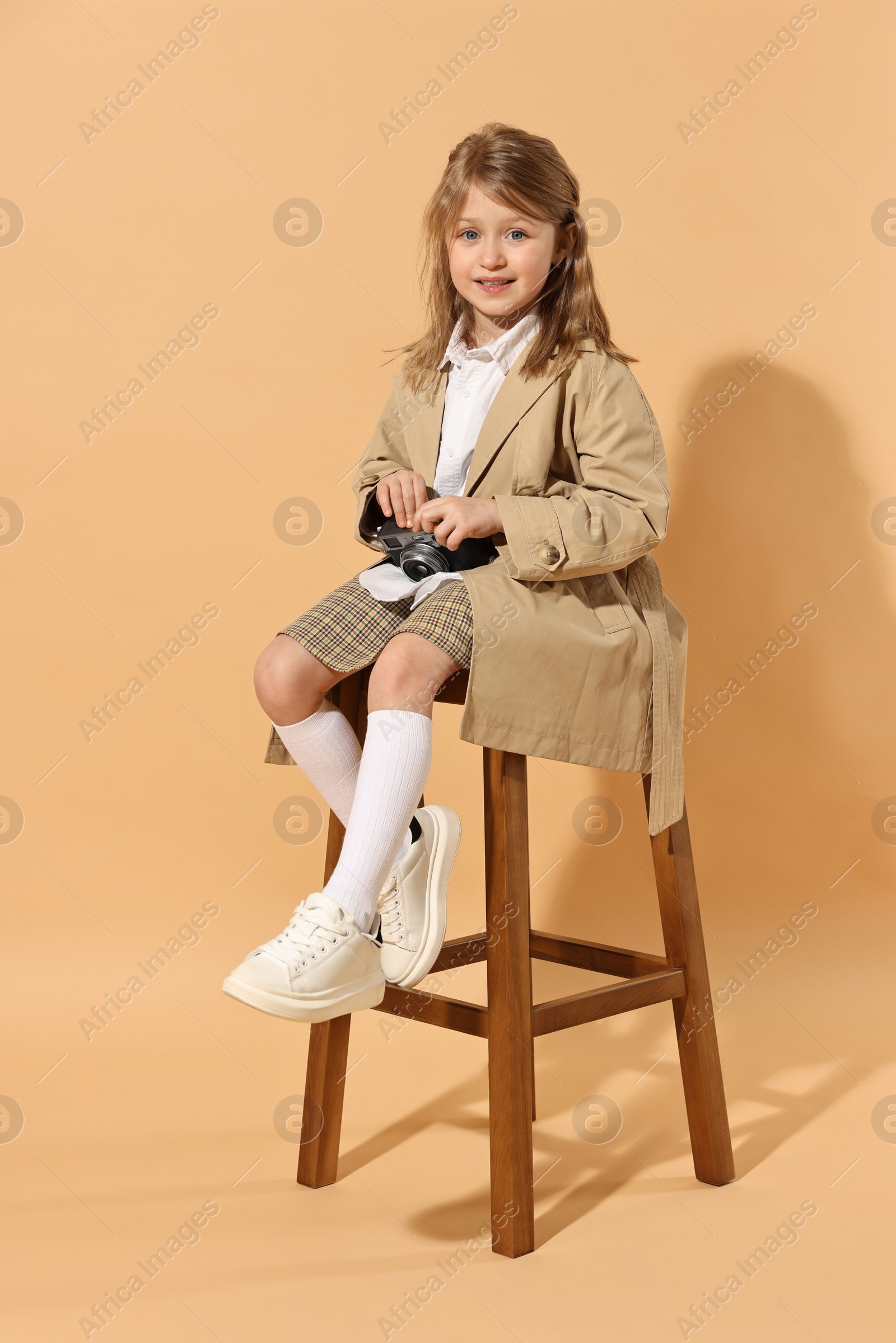 Photo of Fashion concept. Stylish girl with vintage camera on pale orange background