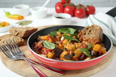 Photo of Dish with tasty ratatouille, bread and basil on wooden board