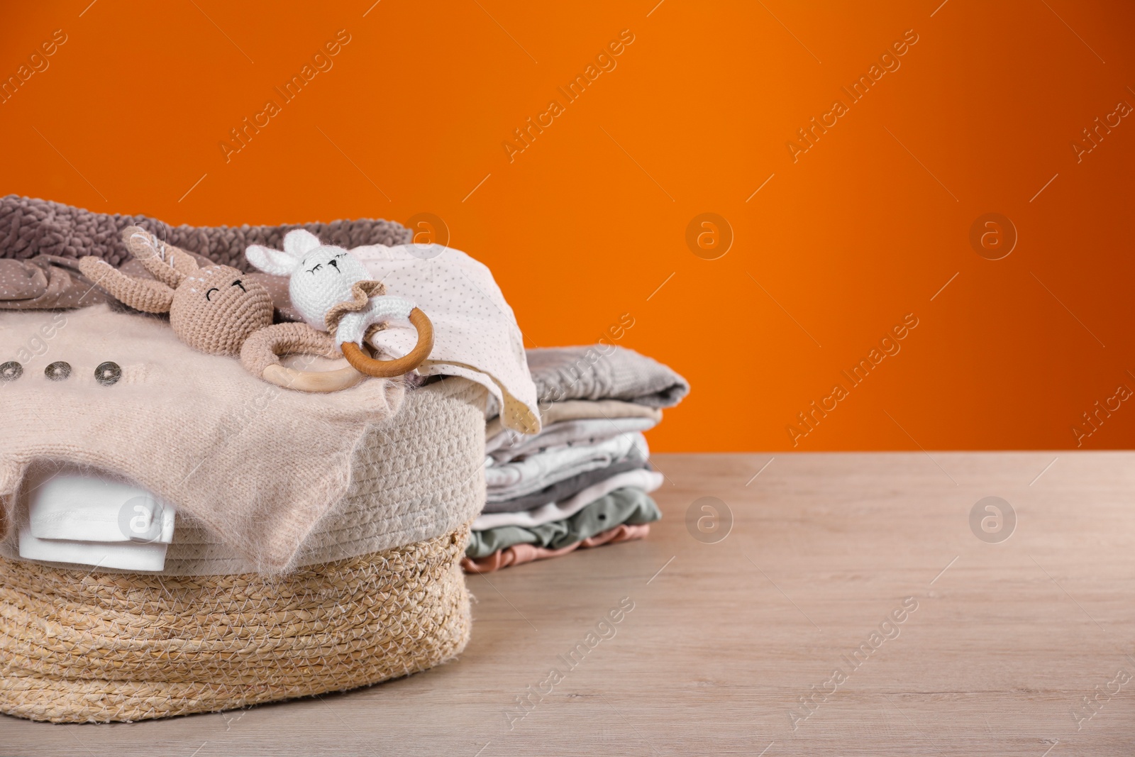 Photo of Laundry basket with baby clothes and crochet toys on wooden table against orange background, space for text