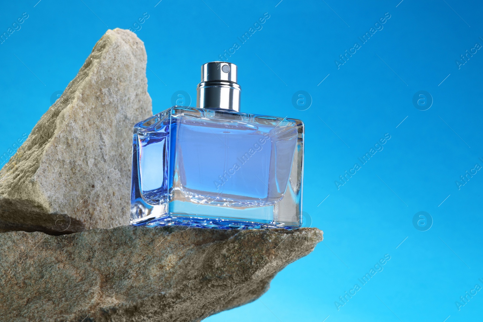 Photo of Stylish presentation of luxury men`s perfume on stones against light blue background. Space for text