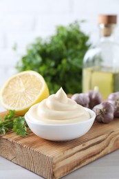 Photo of Tasty mayonnaise sauce in bowl, parsley, garlic and lemon on white wooden table