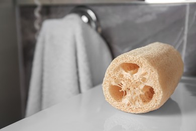 Photo of Natural loofah sponge on white surface in bathroom, closeup. Space for text