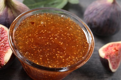 Bowl with tasty sweet jam and fresh figs on grey table, closeup