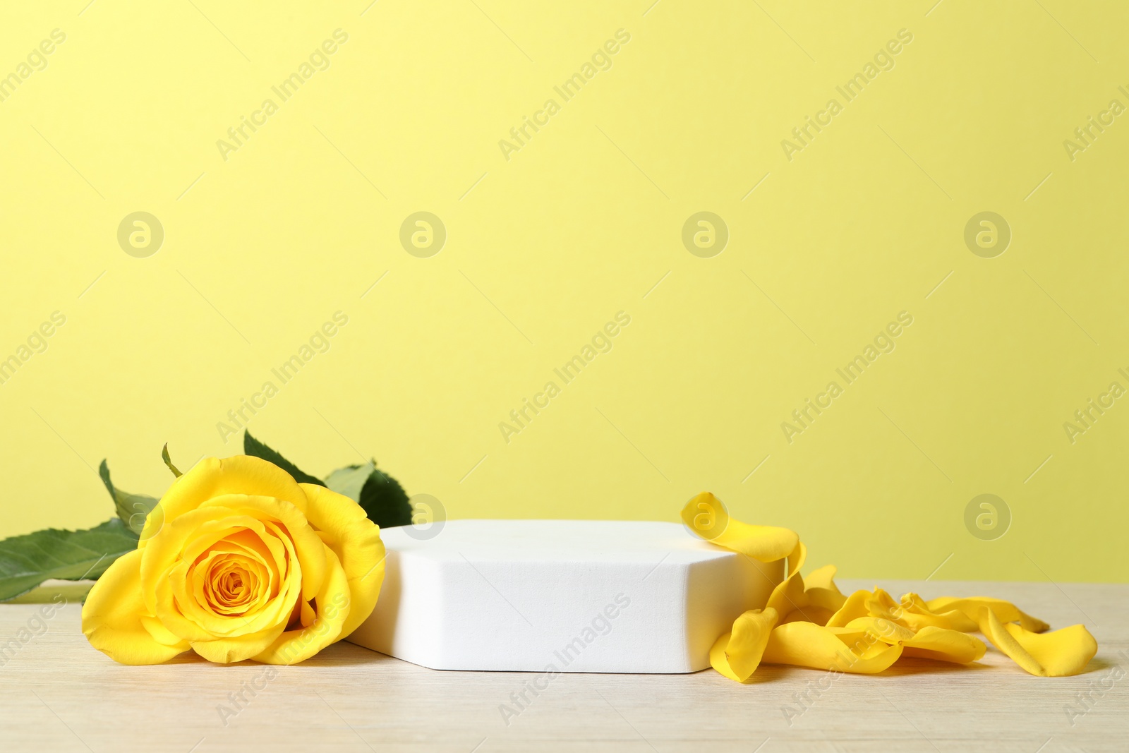 Photo of Beautiful presentation for product. White podium and roses on wooden table against yellow background, space for text