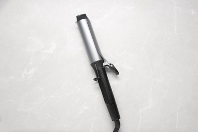 Hair styling appliance. Curling iron on light grey marble table, top view