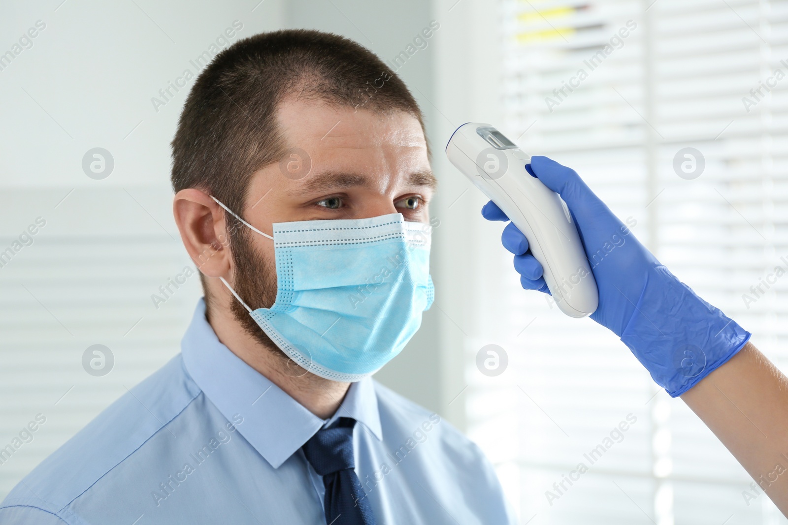 Photo of Doctor measuring patient's temperature with non contact infrared thermometer in office, closeup