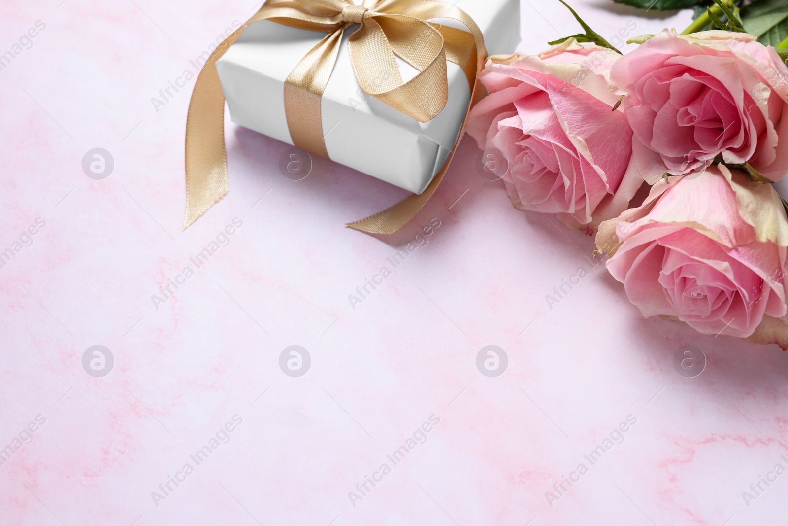 Photo of Beautiful bouquet of roses and gift on light pink marble table, space for text. Happy birthday greetings