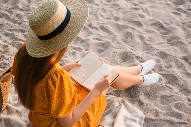 Photo of Young woman reading book on sandy beach, back view