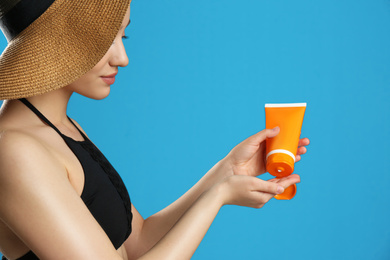 Young woman applying sun protection cream on blue background, closeup