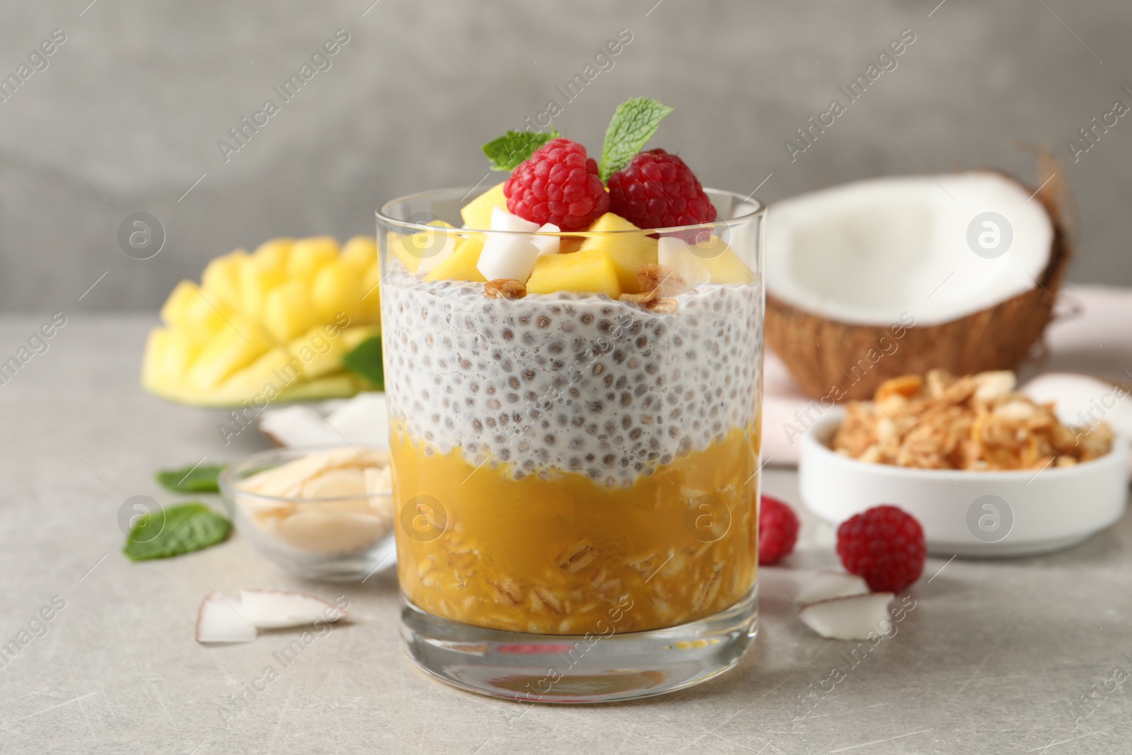 Photo of Delicious chia pudding with mango, raspberries and granola on light grey table