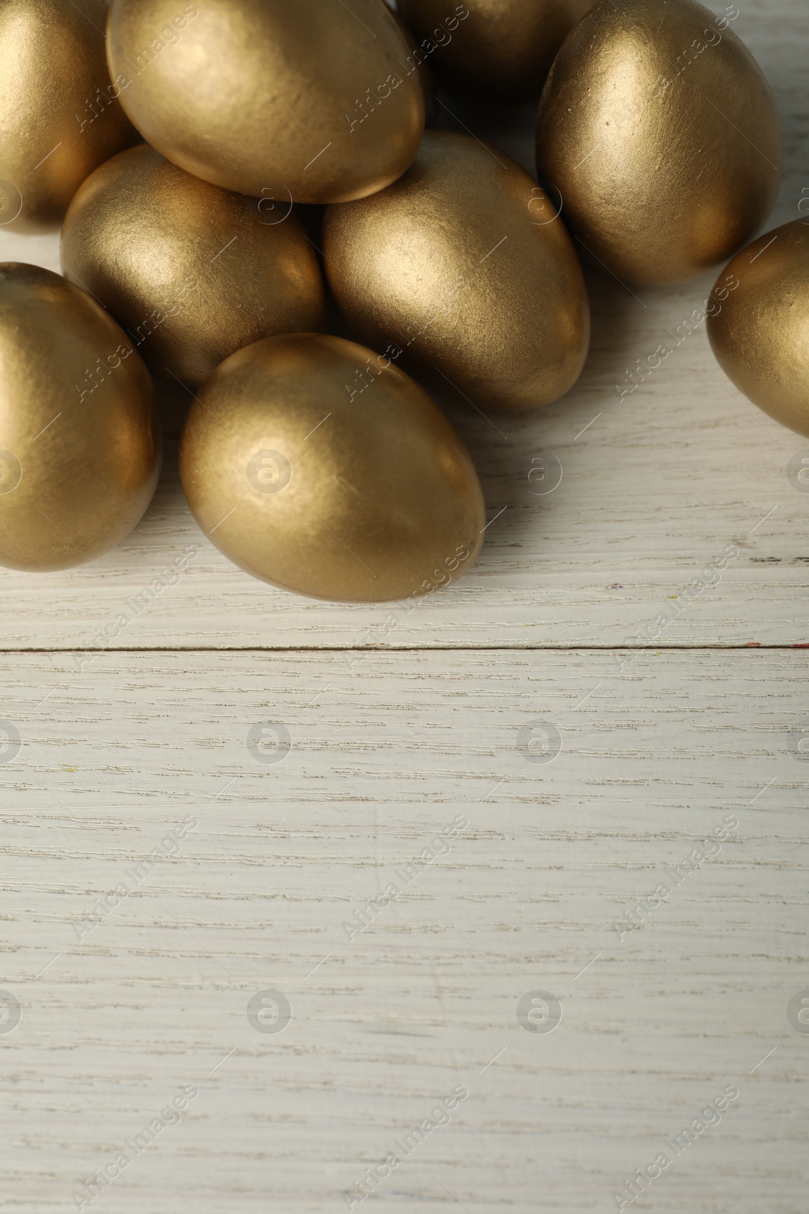 Photo of Shiny golden eggs on white wooden table, top view. Space for text