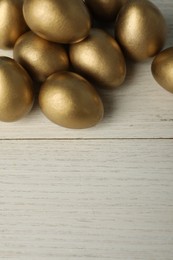 Photo of Shiny golden eggs on white wooden table, top view. Space for text