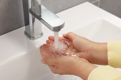 Photo of Woman washing hands with water from tap in bathroom, closeup