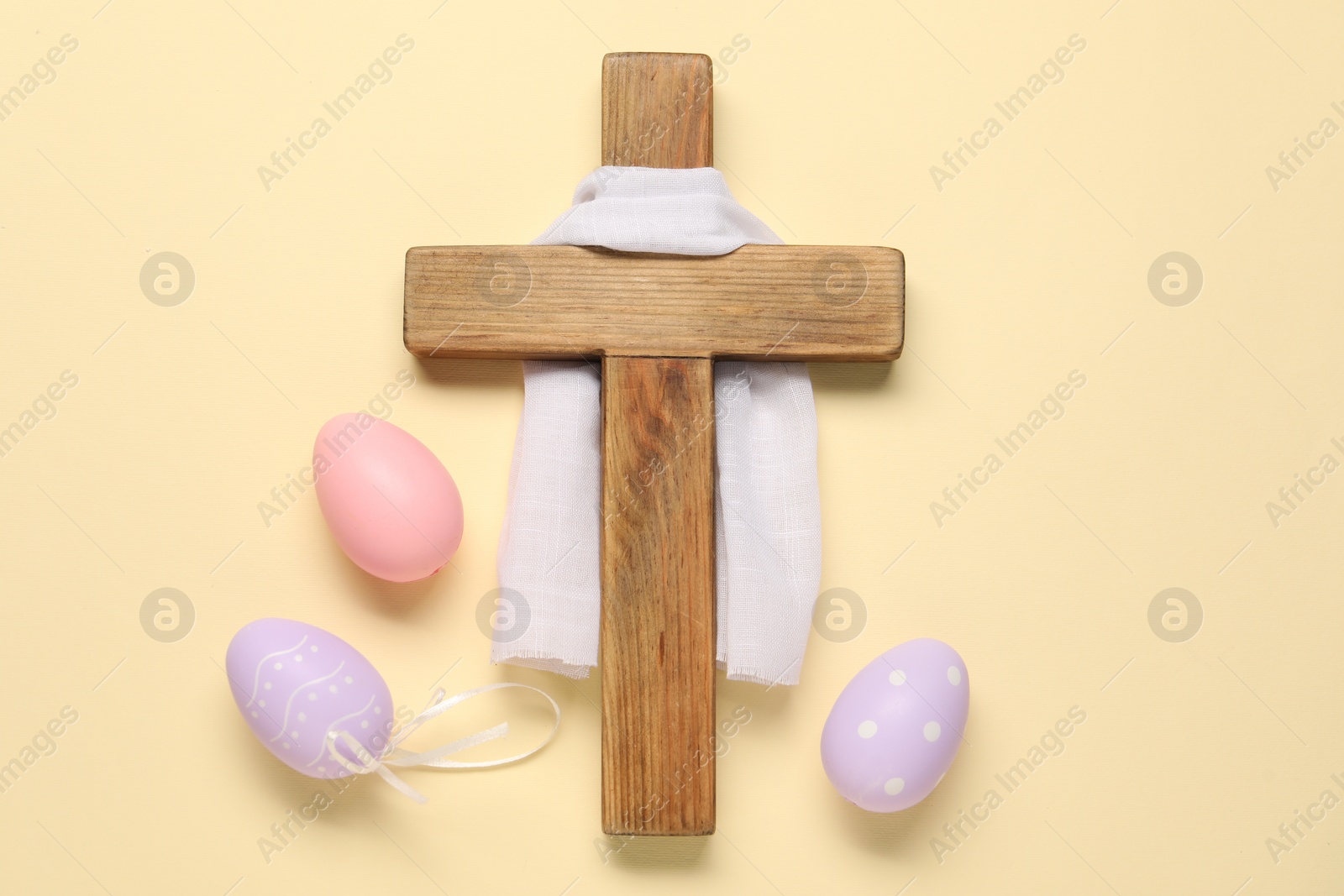 Photo of Wooden cross, white cloth and painted Easter eggs on beige background, flat lay