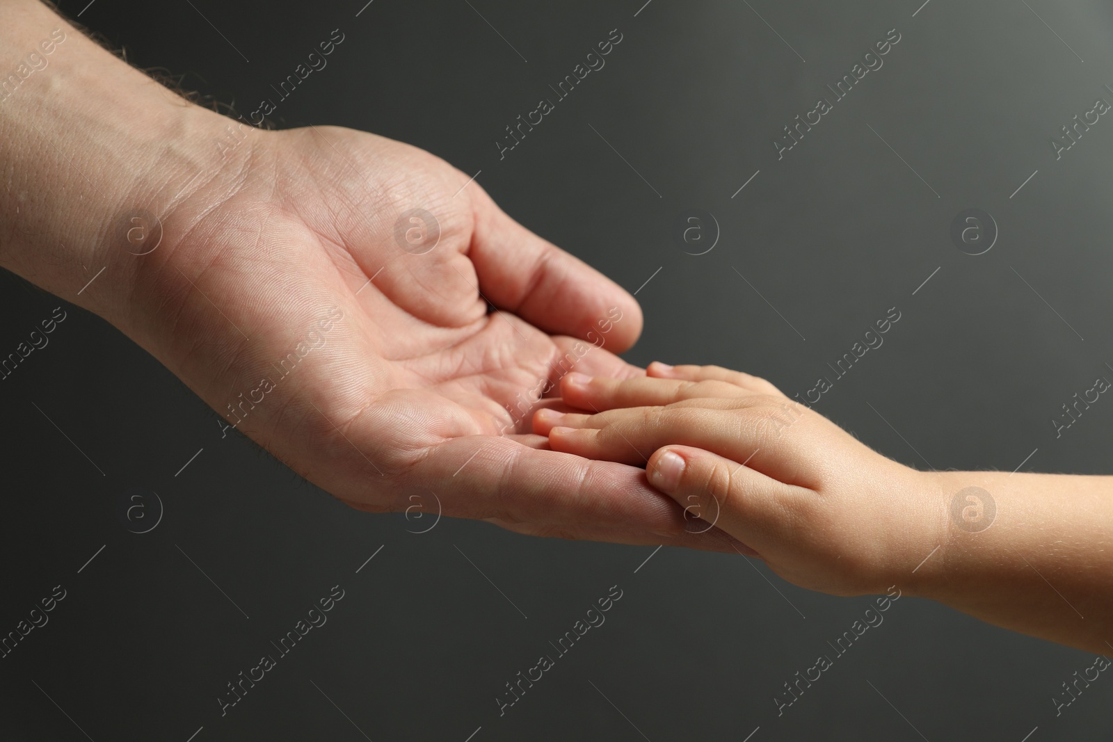 Photo of Father and child holding hands on dark grey background, closeup