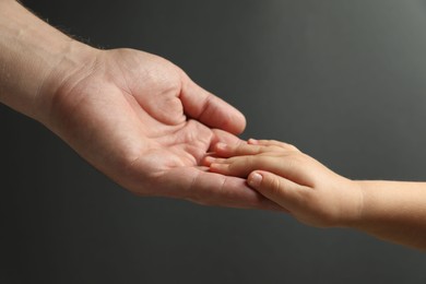 Father and child holding hands on dark grey background, closeup