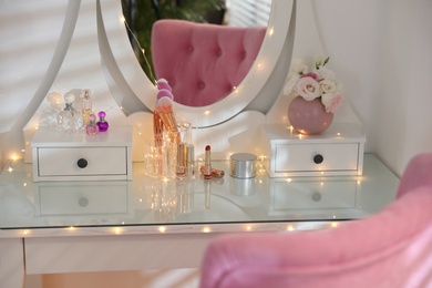 Elegant dressing table with lights and pink chair in stylish room interior