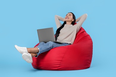 Photo of Happy woman with laptop sitting on beanbag chair against light blue background