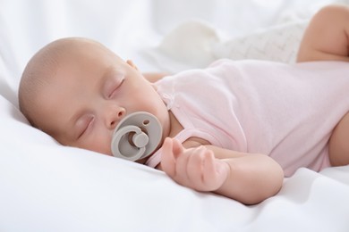 Photo of Cute little baby with pacifier sleeping on bed, closeup