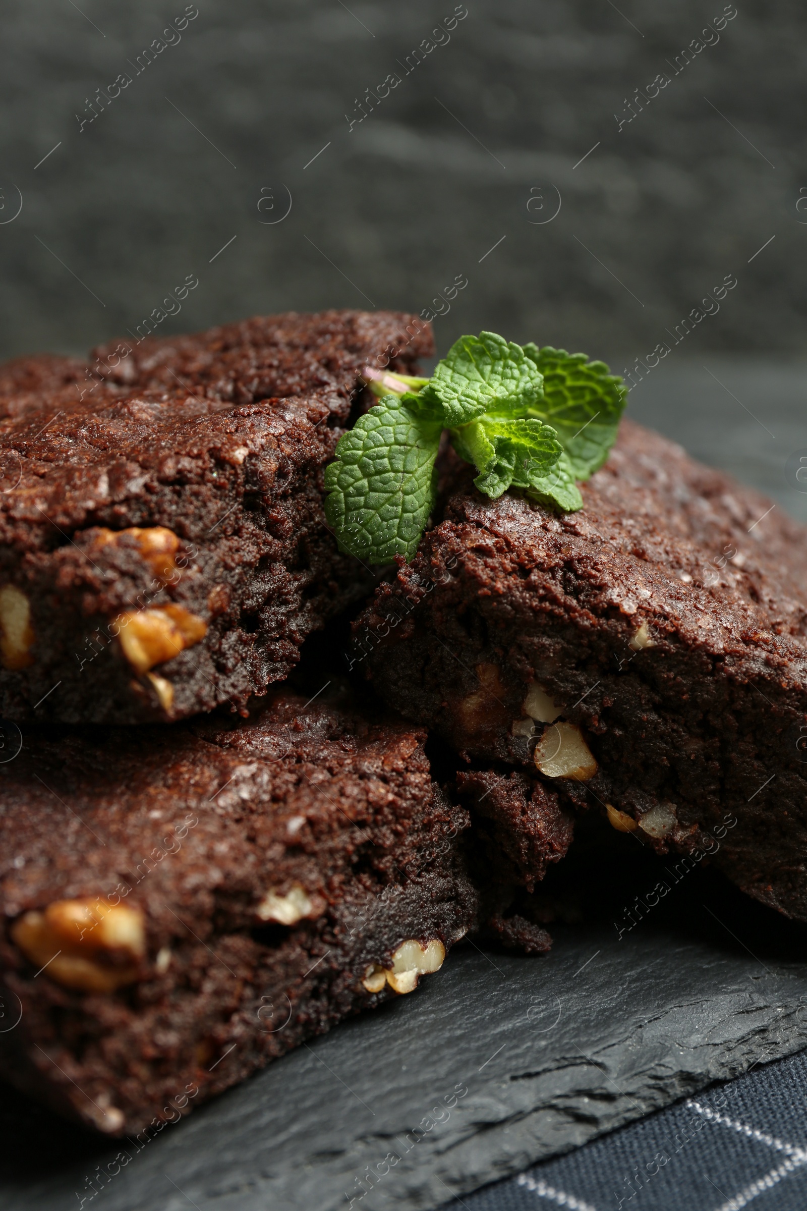 Photo of Delicious chocolate brownies with nuts and fresh mint on slate plate, closeup