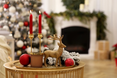 Photo of Christmas composition with decorative reindeer and candles on golden table in room, space for text