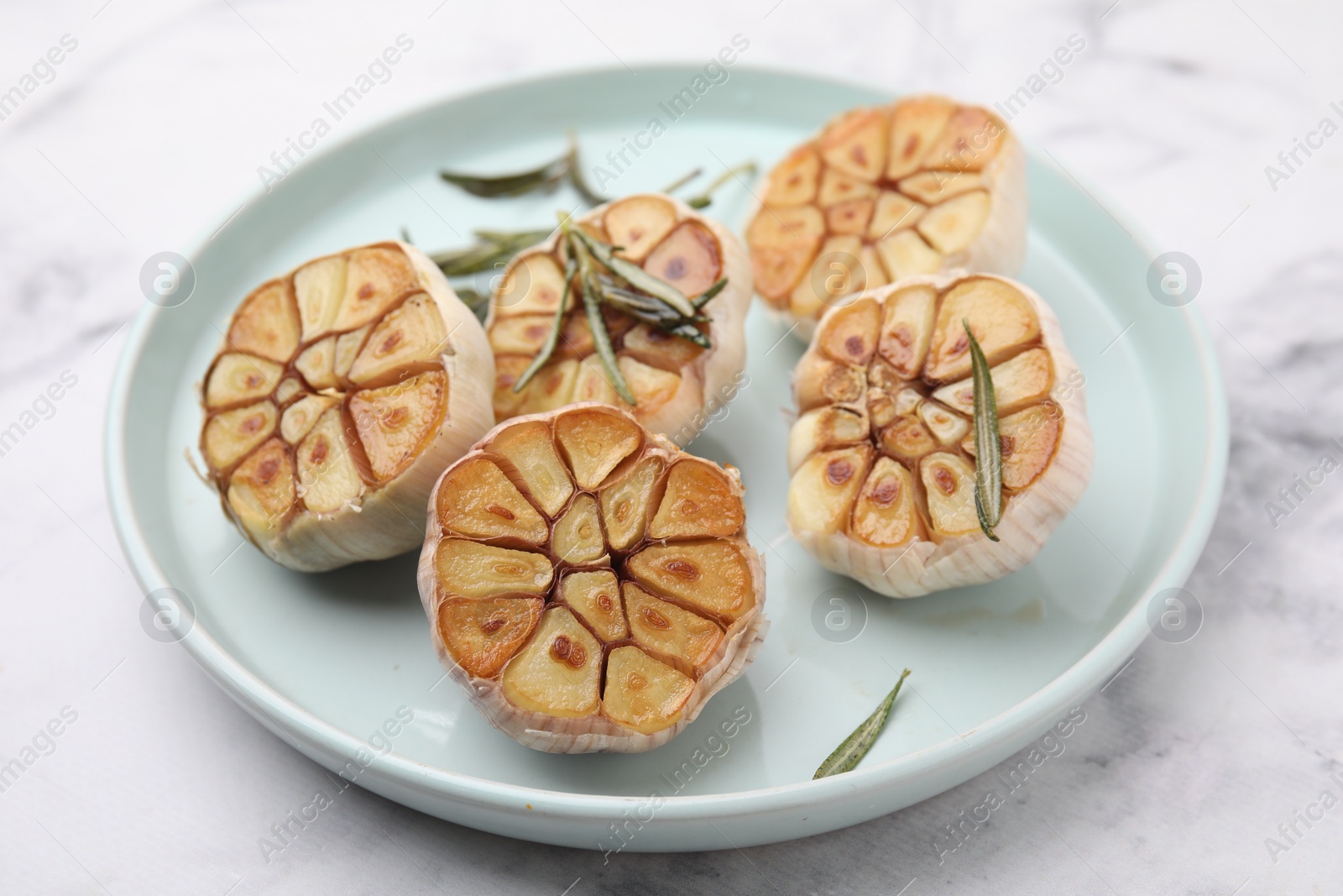 Photo of Heads of fried garlic and rosemary on white table, closeup