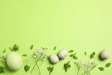 Beautiful flat lay composition with flowers and Easter eggs on green background. Space for text