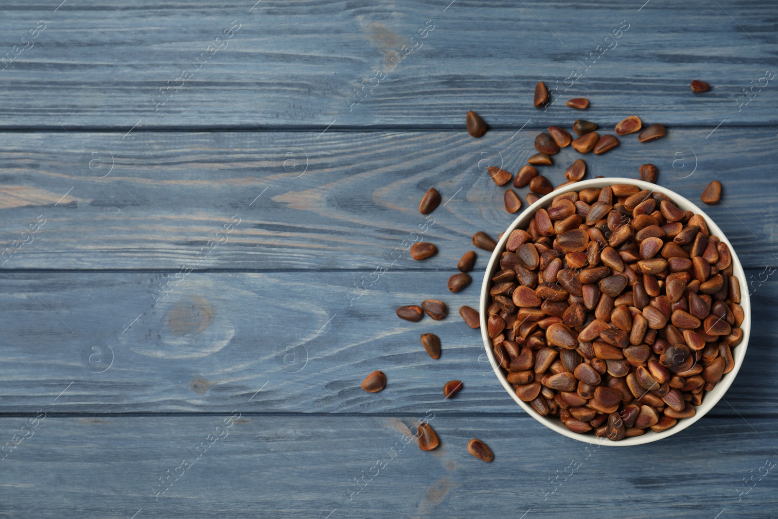 Photo of Bowl with pine nuts and space for text on wooden background, top view