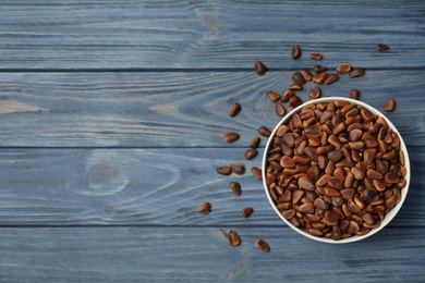 Photo of Bowl with pine nuts and space for text on wooden background, top view