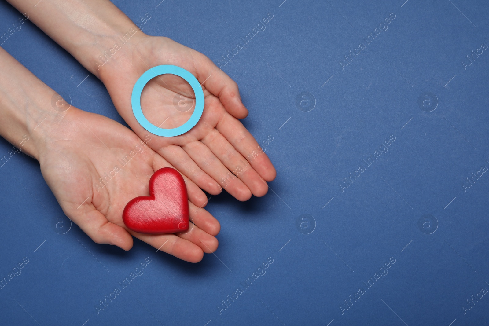 Photo of Woman showing blue paper circle as World Diabetes Day symbol and red heart on color background, top view with space for text