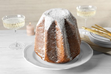 Photo of Delicious Pandoro cake decorated with powdered sugar and sparkling wine on white wooden table. Traditional Italian pastry