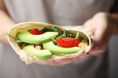 Photo of Woman holding delicious hummus wrap with vegetables, closeup